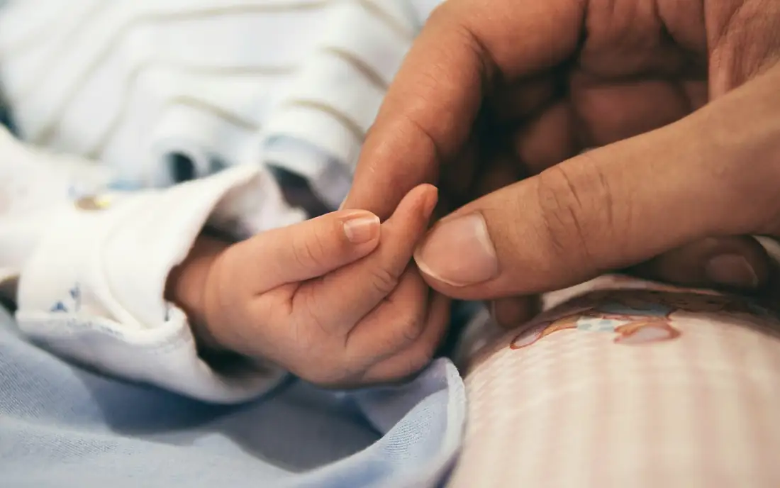 A parent's hand holding a newborn's hand