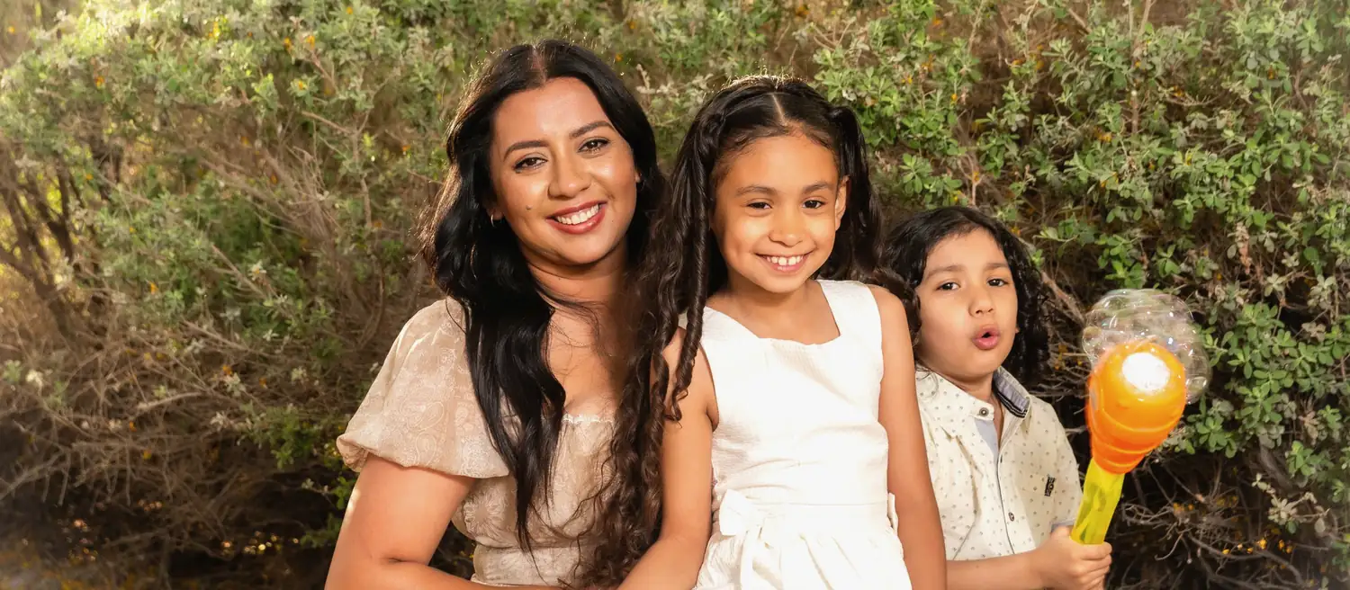 Una madre y sus dos hijos pequeños sonriendo al aire libre
