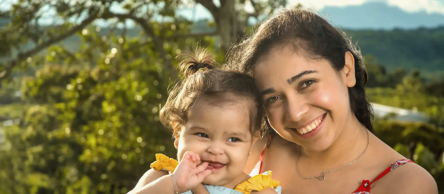 A mother holding her baby outdoors in the sunshine