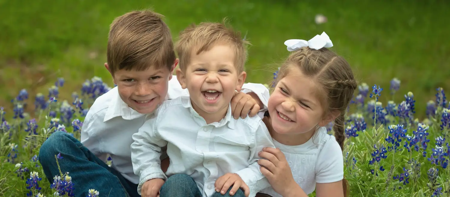 Tres niños riendo juntos en un campo de bluebonnets