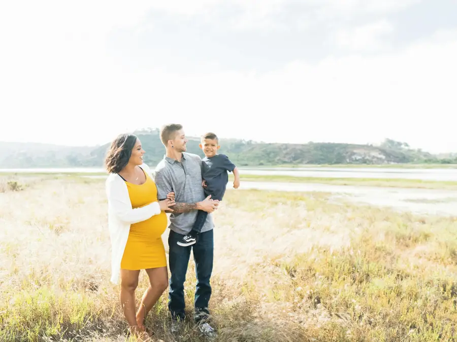A couple expecting a baby, with their young son, standing together in an open field
