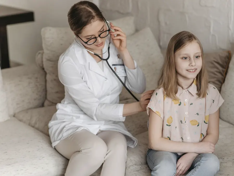 A doctor listening to a smiling child's heart at home
