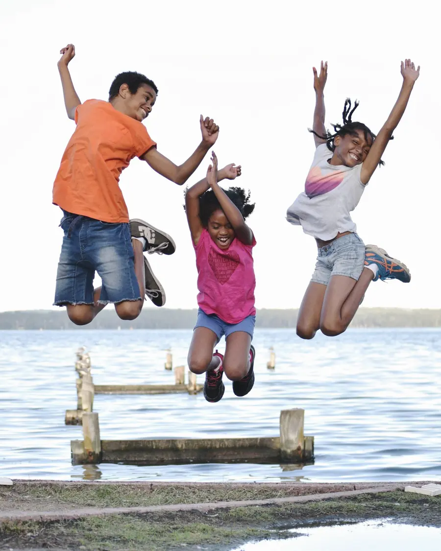 Children jumping off a dock with their arms raised
